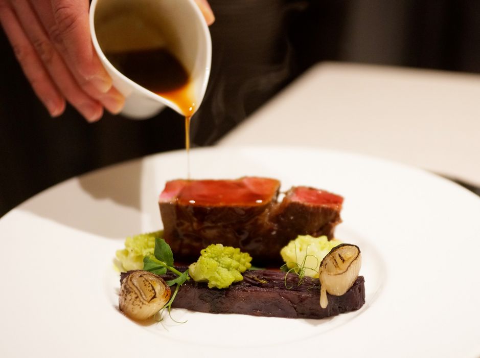 Salsa versata su filetto di carne con contorni di verdure su piatto bianco.