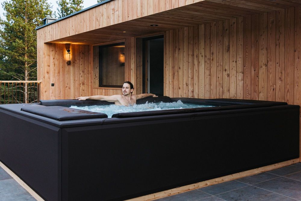 Uomo che si rilassa in una vasca idromassaggio esterna su un terrazzo di legno Uomo che si rilassa in una vasca idromassaggio esterna su un terrazzo di legno