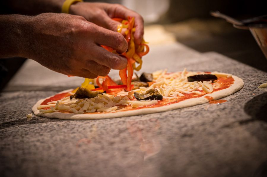 Hands adding sliced bell peppers on a pizza with cheese and mushrooms