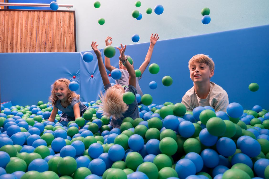 Bambini che giocano in una piscina di palline blu e verdi in un'area giochi al chiuso.