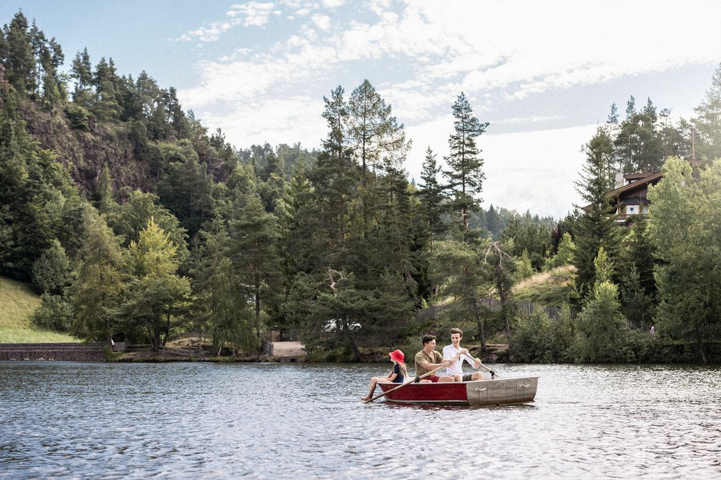 Persone su una barca a remi in un lago circondato da alberi e colline