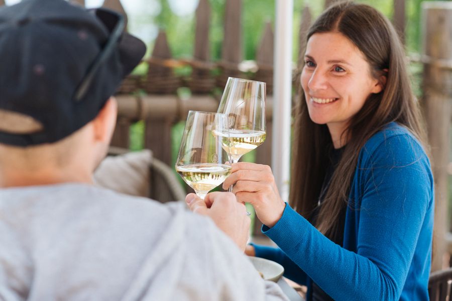 Due persone brindano con calici di vino bianco all'aperto, una donna sorride felice.