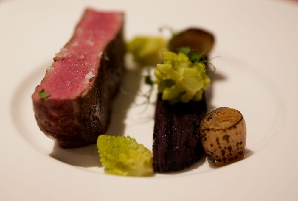 Piatto con bistecca al sangue, cavolfiore e cipolla caramellata su piatto bianco.