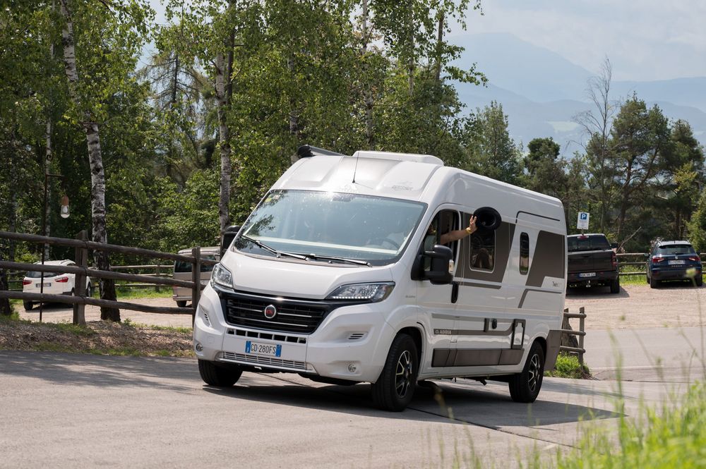 Weißer Wohnmobil-Kleinbus auf einer Straße mit einer Hand, die einen Hut aus dem Fenster hält.