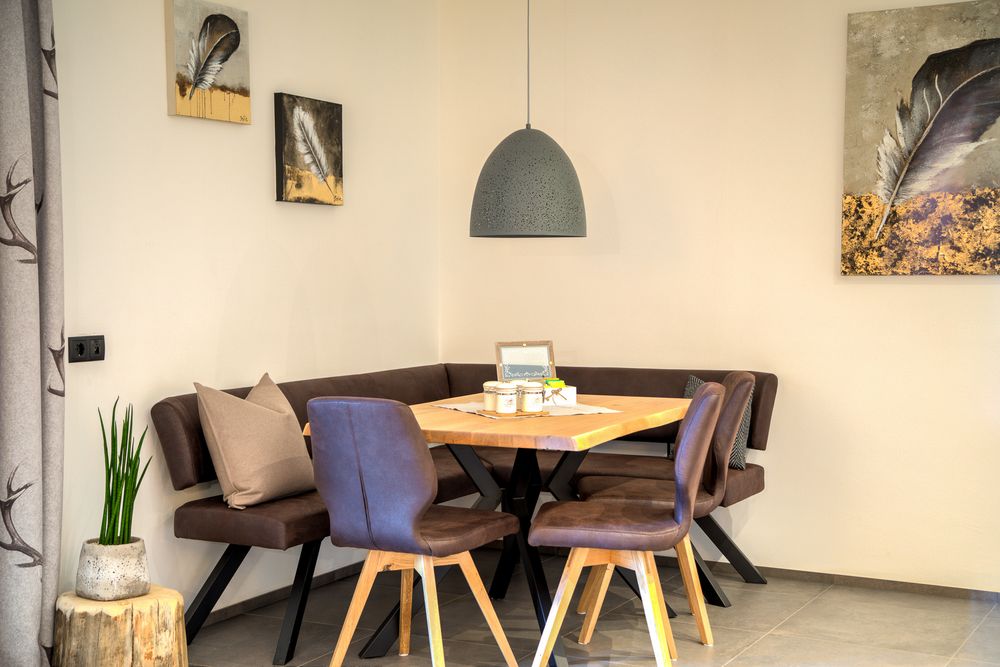 Cozy dining corner with wooden table, brown cushioned chairs, feather paintings on walls, and a potted plant on a wooden stump. Cozy dining corner with wooden table, brown cushioned chairs, feather paintings on walls, and a potted plant on a wooden stump.