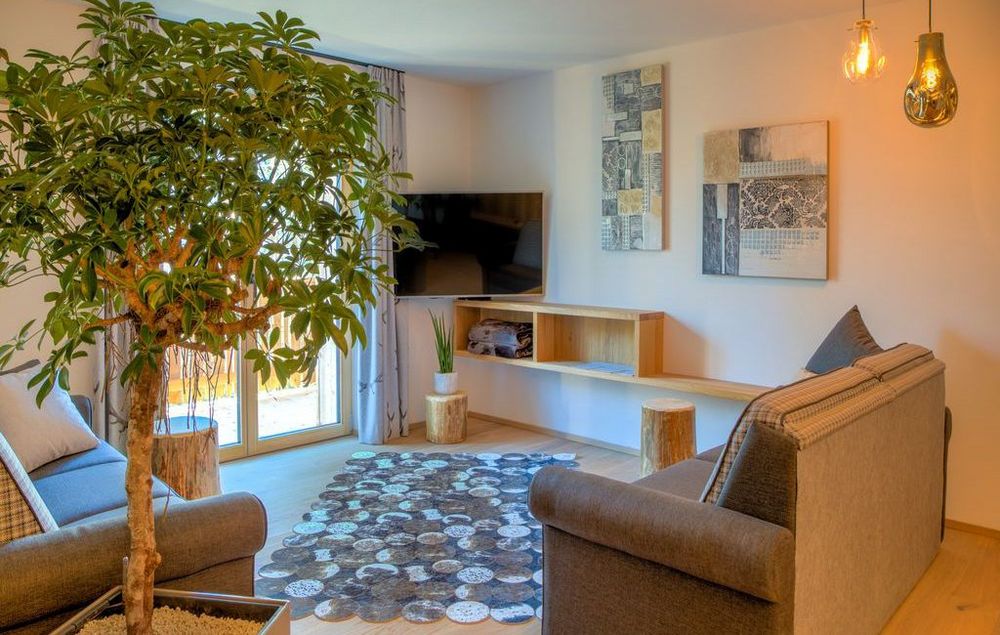 Cozy living room with two sofas, patterned rug, potted tree, wall-mounted TV, and abstract wall art.