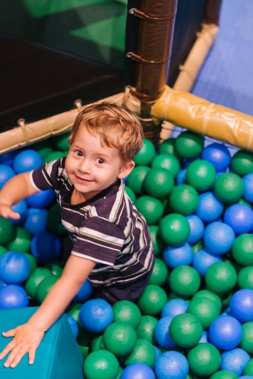 Bambino che gioca in una piscina di palline verdi e blu.