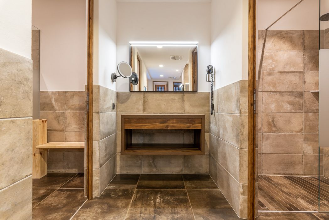 Bagno moderno con piastrelle beige, specchio illuminato e mobili in legno