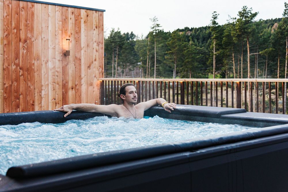 Mann entspannt in Whirlpool auf Terrasse mit Blick auf Bäume