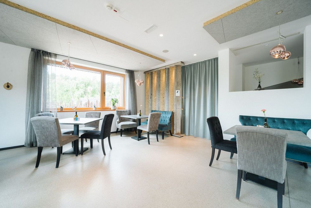 Interno di un moderno ristorante con tavoli e sedie imbottite, grandi finestre e luci sospese.