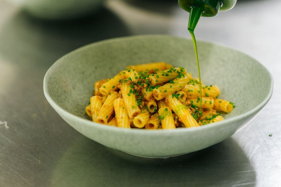 Pasta rigata con sugo e erba cipollina in una ciotola con olio verde versato sopra.