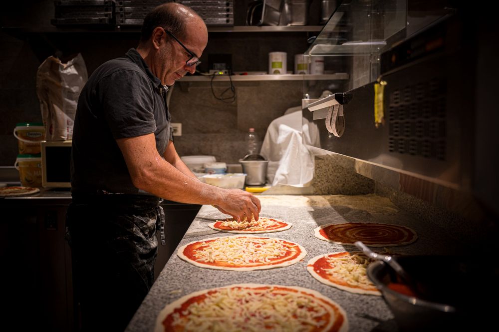 A man preparing multiple pizzas with cheese on a kitchen counter.
