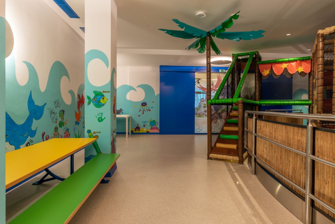 Area giochi per bambini con tavolo colorato e struttura a tema tropicale con palme finte