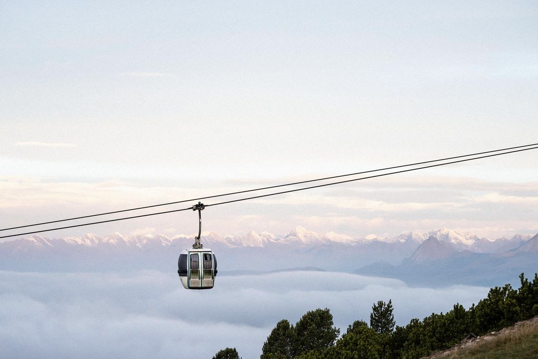 Cabina di funivia sospesa sopra una valle nebbiosa con montagne innevate sullo sfondo