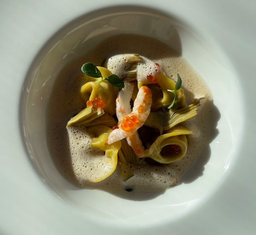 Piatto elegante con tortellini, gamberi, carciofi, uova di pesce e salsa schiumosa.
