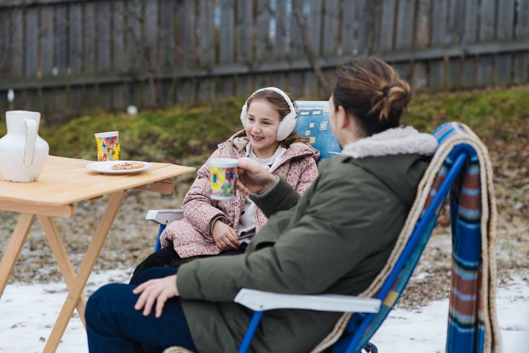 Due persone sedute all'aperto con tazze colorate in mano, vestite con abiti invernali.