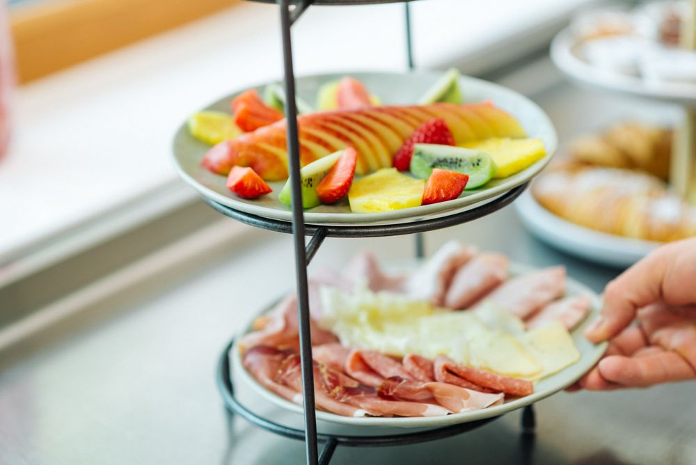 Vassoio a due piani con frutta fresca in alto e affettati con formaggi in basso