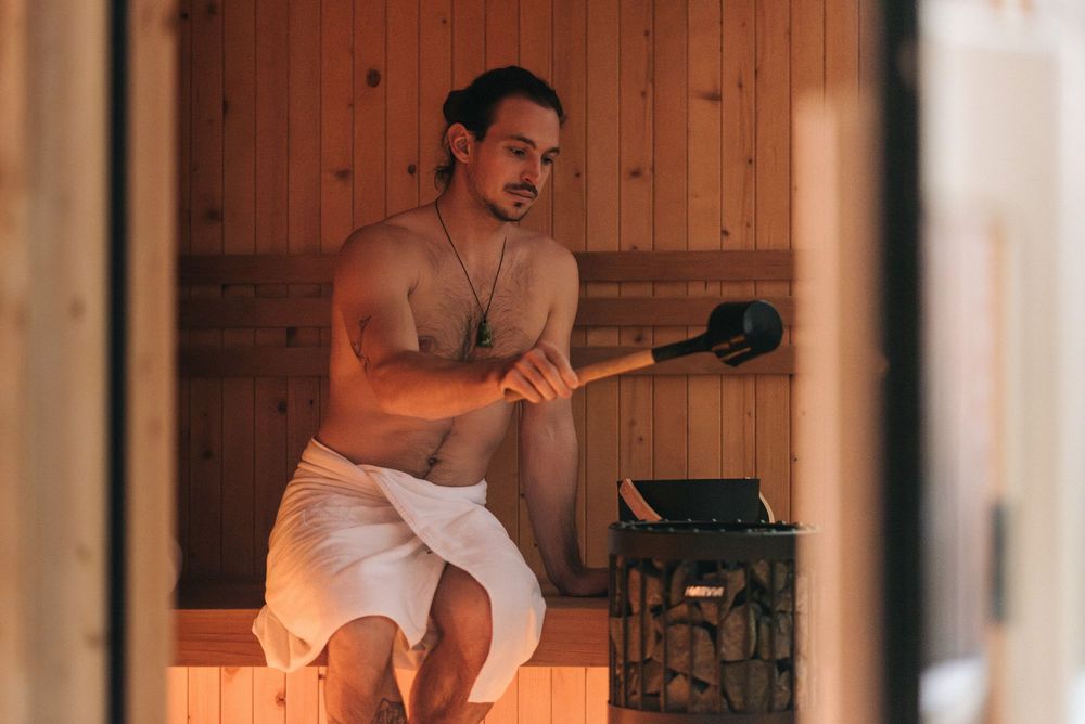 Mann sitzt in Sauna und gießt Wasser auf heiße Steine.