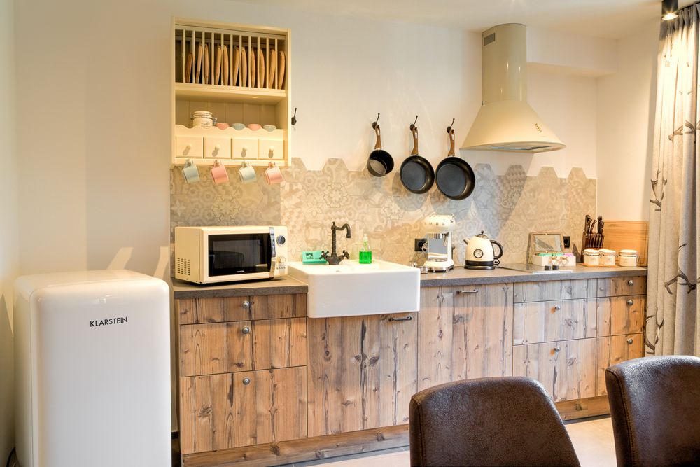 Modern kitchen with wooden cabinets, white sink, hanging pans, microwave, and vintage-style fridge.
