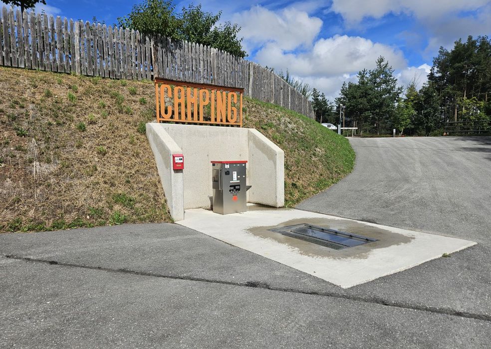 Area di servizio per campeggio con cartello arancione e pavimento in cemento sotto un cielo parzialmente nuvoloso