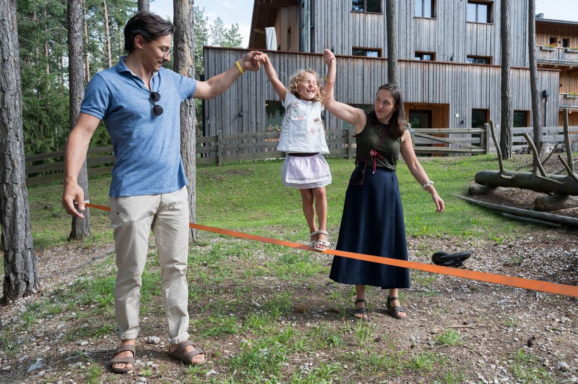 Bambina che cammina su una fune con il sostegno di due adulti all'aperto.