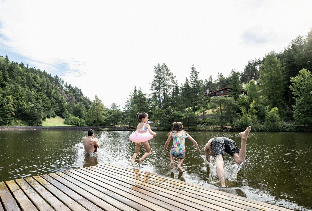 Bambini che saltano in un lago da un pontile di legno in una giornata soleggiata.