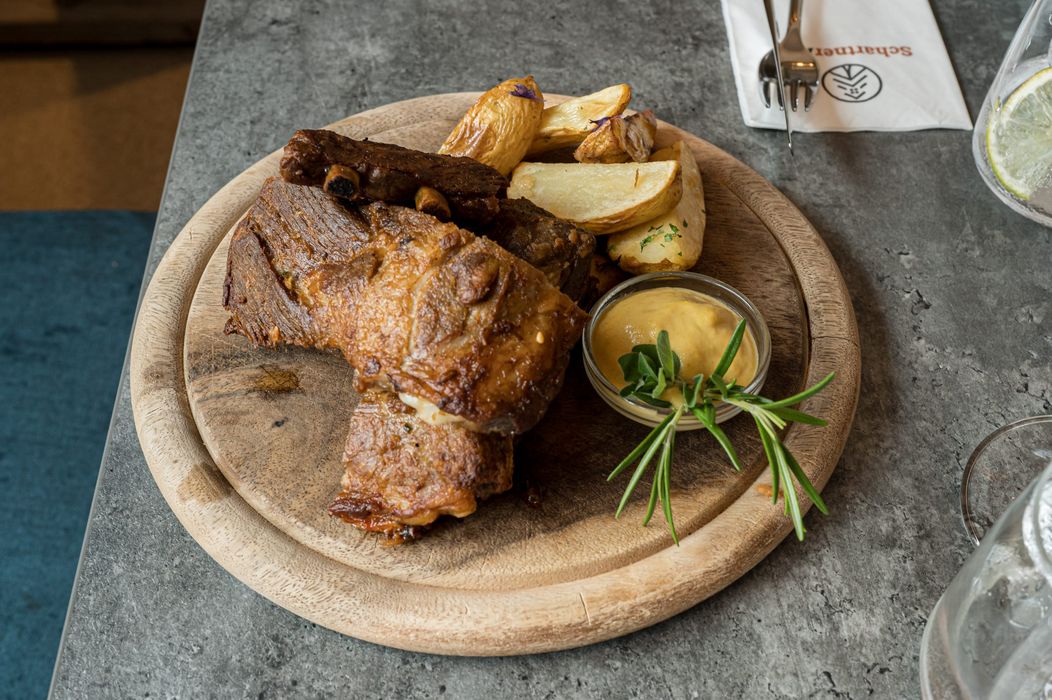 Piatto di carne arrosto con patate e salsa su tagliere di legno.