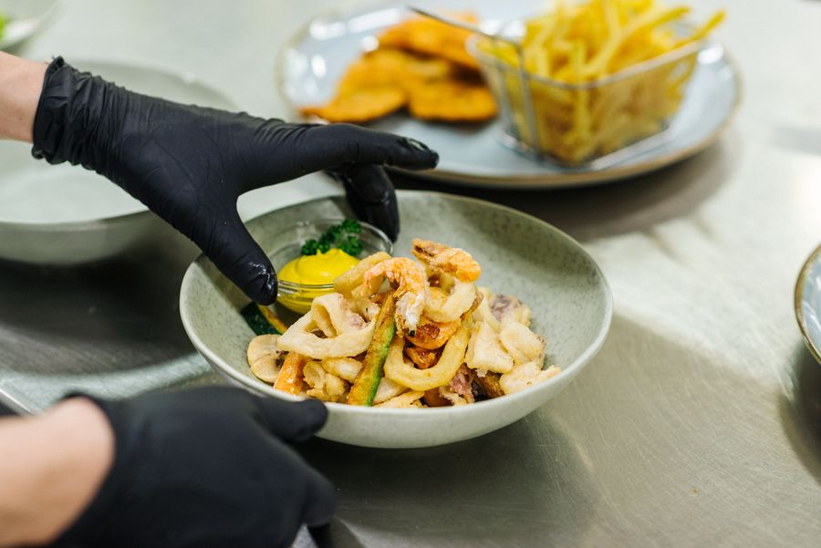 Primo piano di piatto con frittura mista di pesce e salsa gialla con guantoni neri