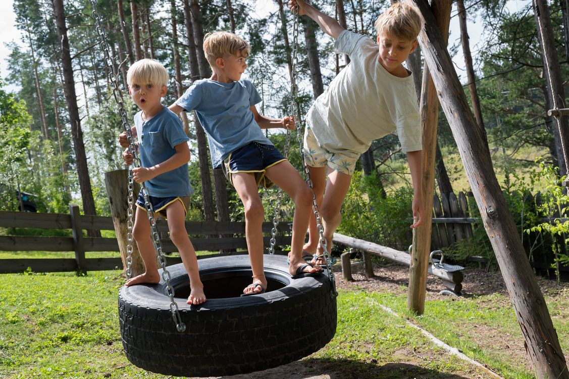Tre bambini giocano su un'altalena a pneumatico all'aperto in un parco con alberi