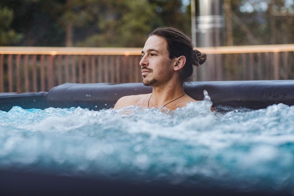 Uomo rilassato con capelli raccolti in una vasca idromassaggio all'aperto