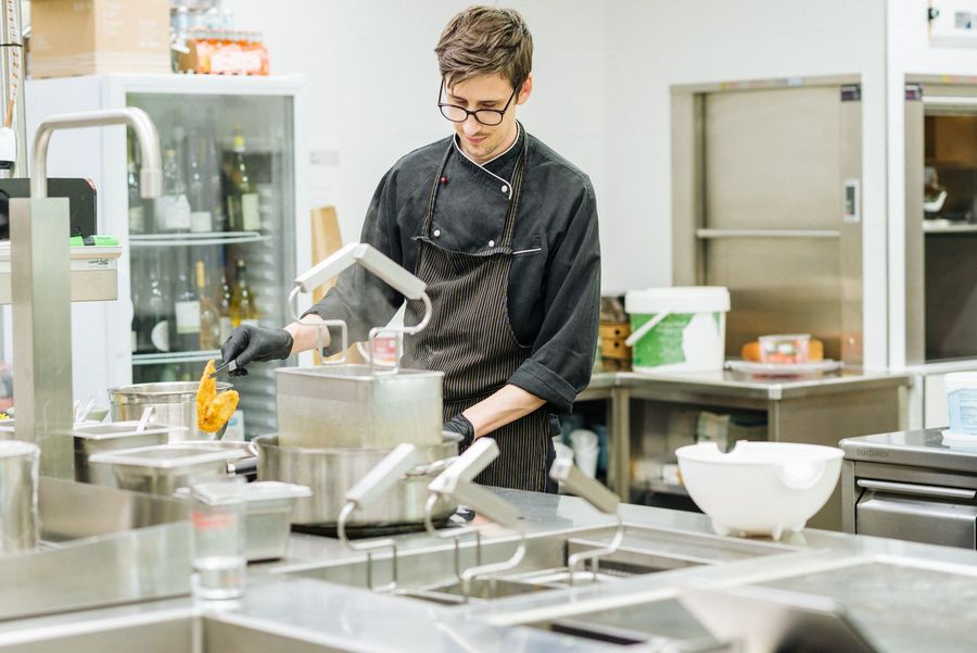 Cuoco in cucina professionale che frigge un alimento in olio bollente