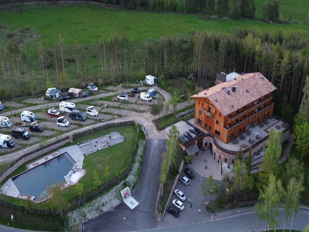 Luftaufnahme eines Campingplatzes neben einem großen Holzhaus mit angrenzendem Wald und Teich.
