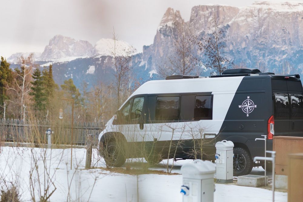Campervan im Winter vor verschneiten Bergen und Bäumen