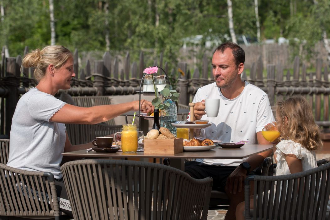 Famiglia che fa colazione all'aperto con succhi, caffè e dolci
