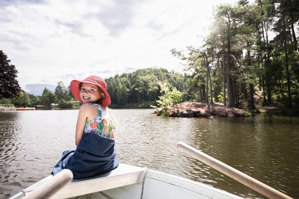 Ragazza sorridente con cappello rosso su una barca in un lago circondato da alberi