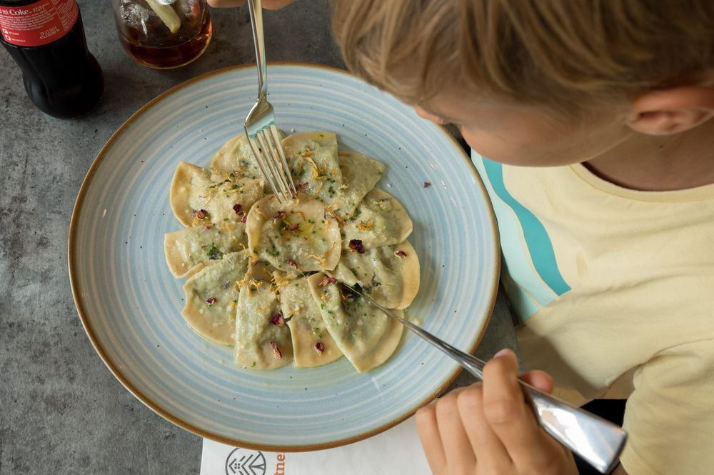 Bambino che mangia ravioli con posate e bevanda cola su tavolo.