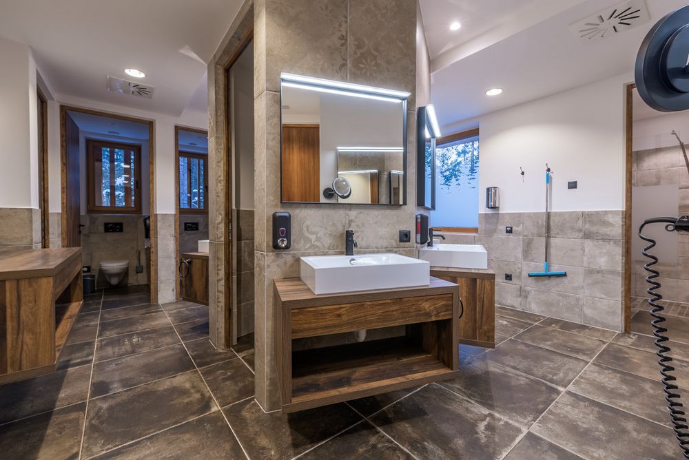 Modernes Badezimmer mit Waschbecken, Spiegeln und WC, naturfarbene Fliesen und Holzdetails