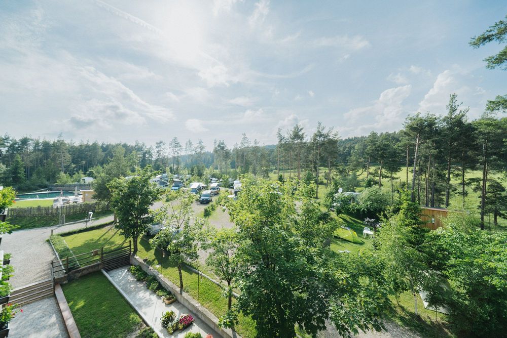 Campeggio verde con tende e camper circondato da alberi sotto un cielo sereno con nuvole.
