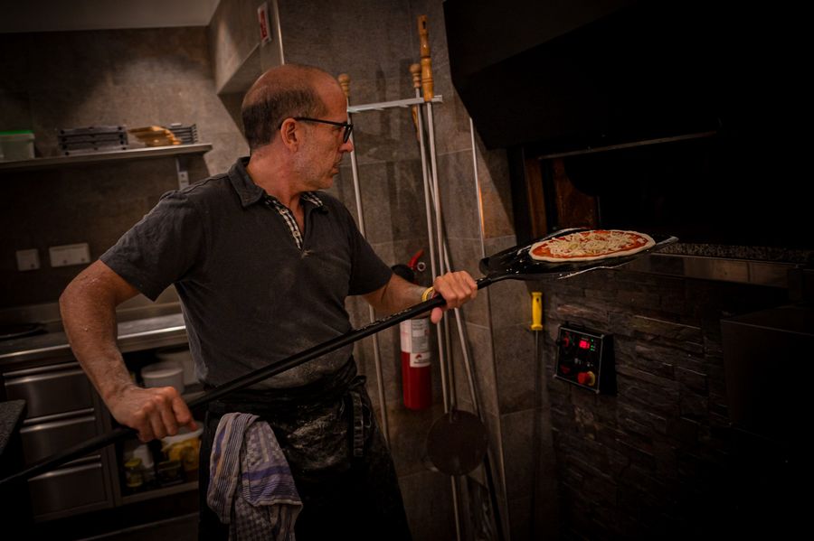 Man placing pizza into a stone oven with a pizza peel.