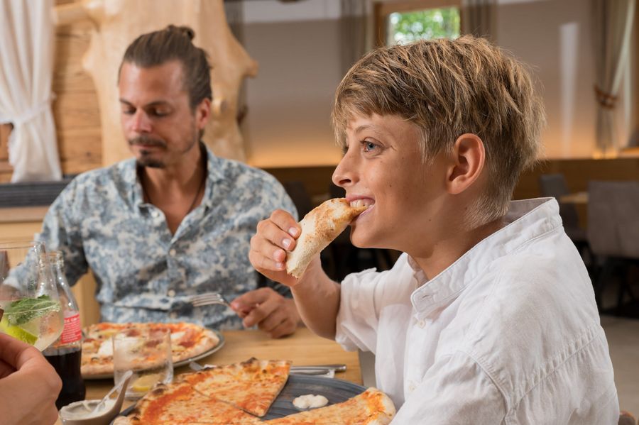 A young boy eating pizza with a man sitting at the table in a restaurant.