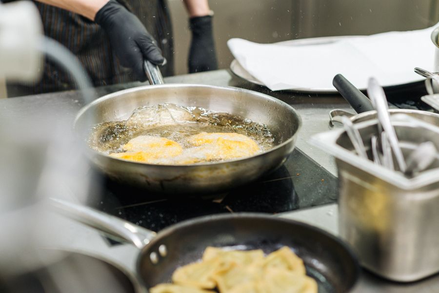 Cibo in fase di frittura in una padella su un piano cottura in cucina professionale.
