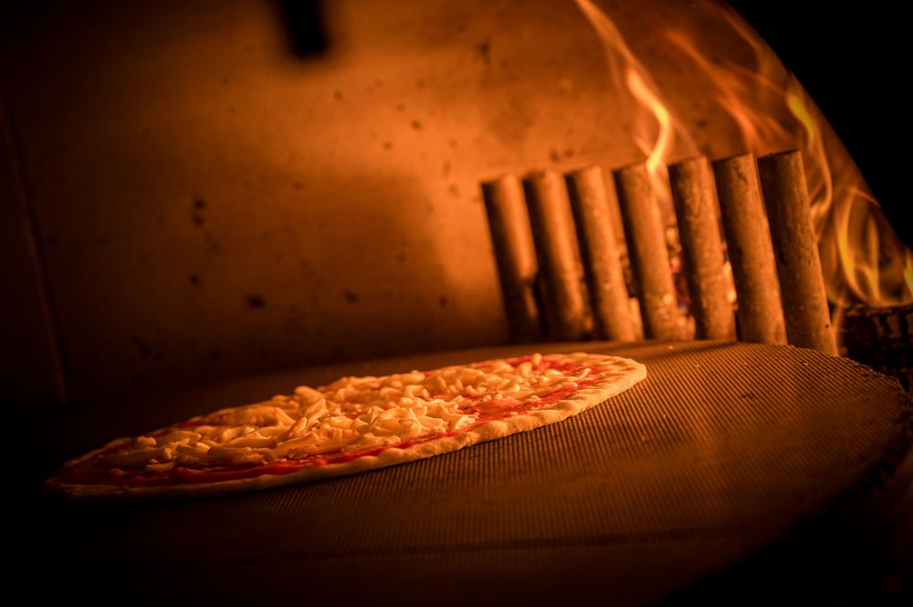 Pizza with cheese baking inside a wood-fired oven with flames.