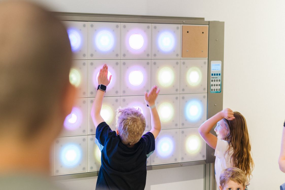 Bambini giocano con un pannello di luci colorate interattive su una parete.