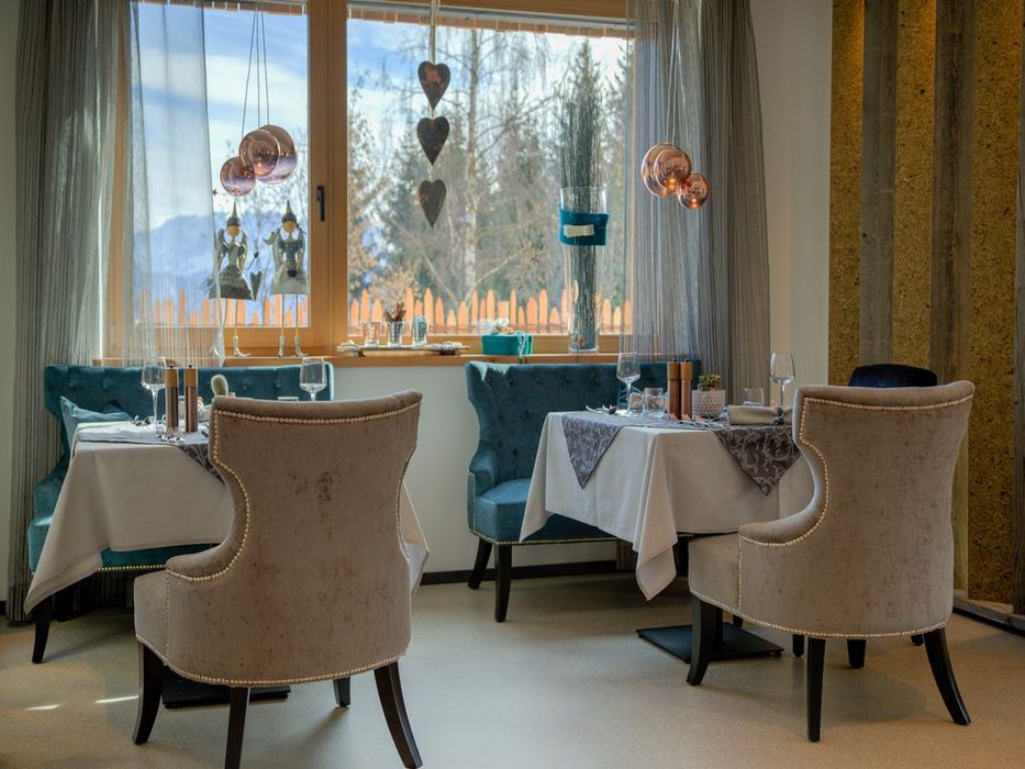 Interno elegante di un ristorante con tavoli apparecchiati e sedie imbottite vicino a una finestra grande.