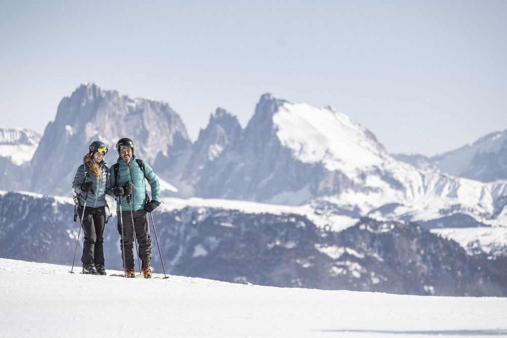 Couple skiing on a snowy mountain with a backdrop of rugged, snow-covered peaks