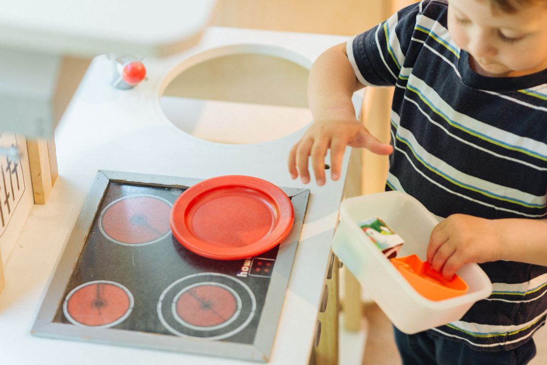 Bambino che gioca con una cucina giocattolo e piatto rosso