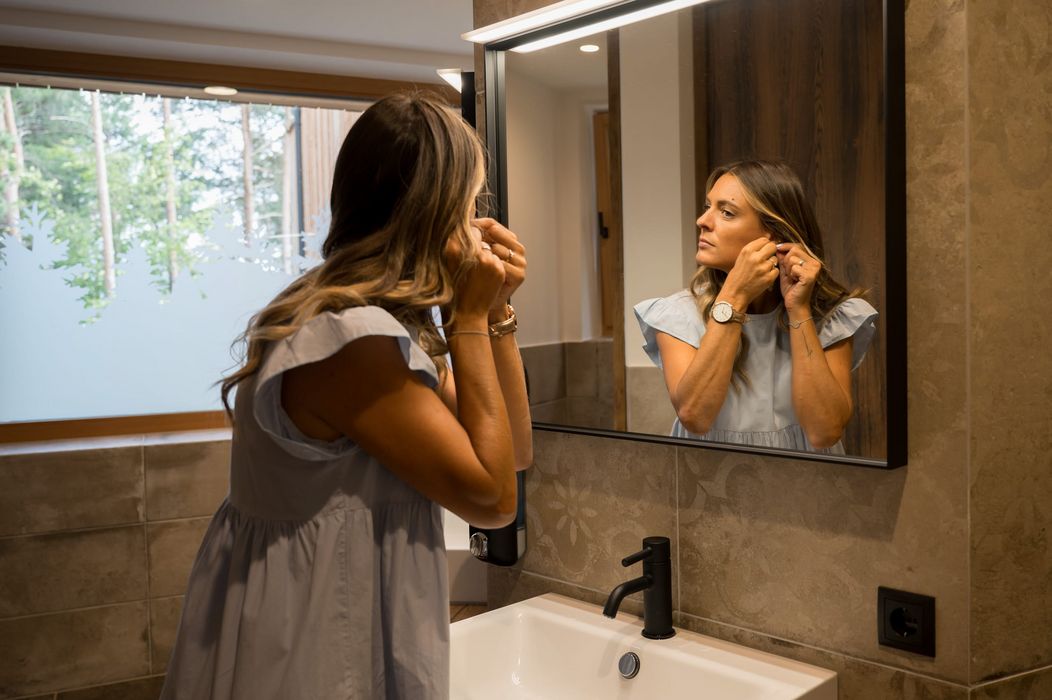 Donna che si mette gli orecchini davanti allo specchio del bagno.