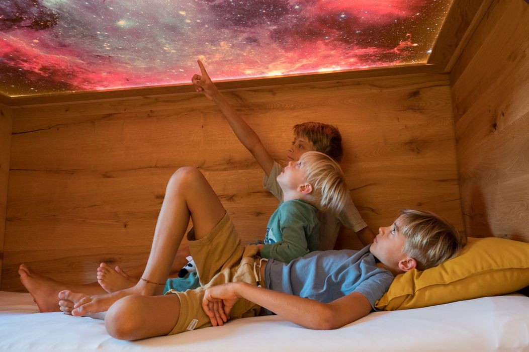 Tre bambini sdraiati guardano un soffitto illuminato con immagini galattiche colorate.