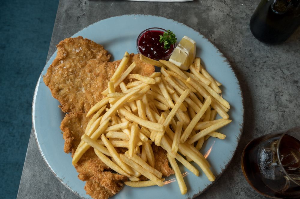 Cotoletta impanata con patatine fritte, salsa rossa e spicchio di limone su un piatto azzurro