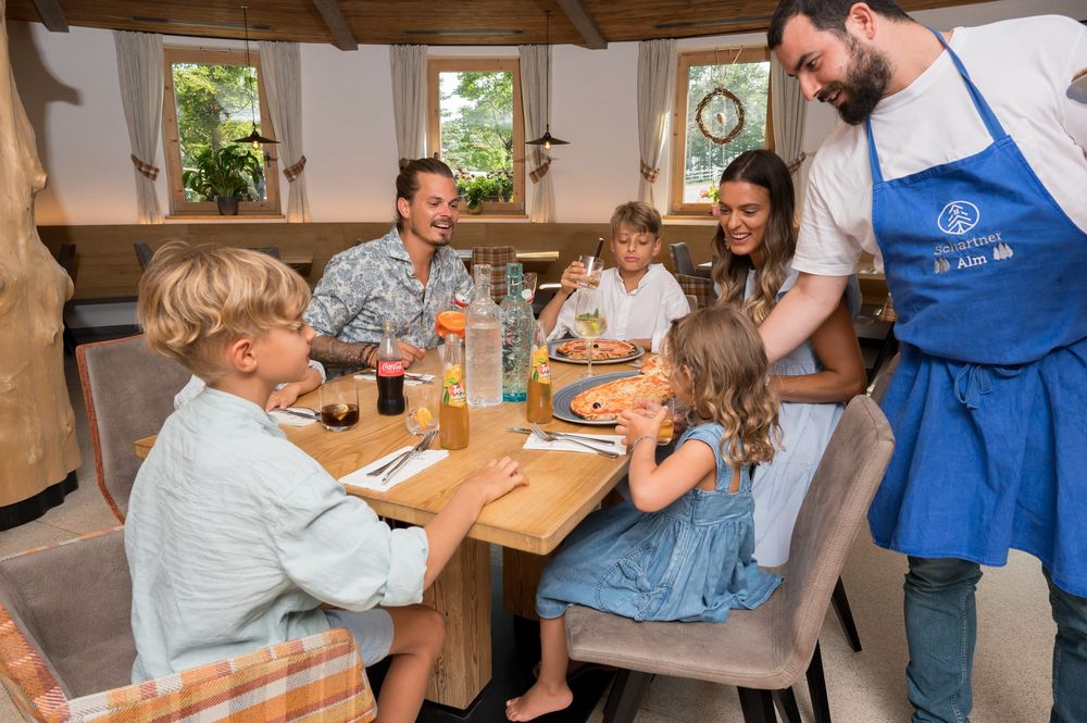 Family enjoying pizza at a restaurant with a waiter serving food.